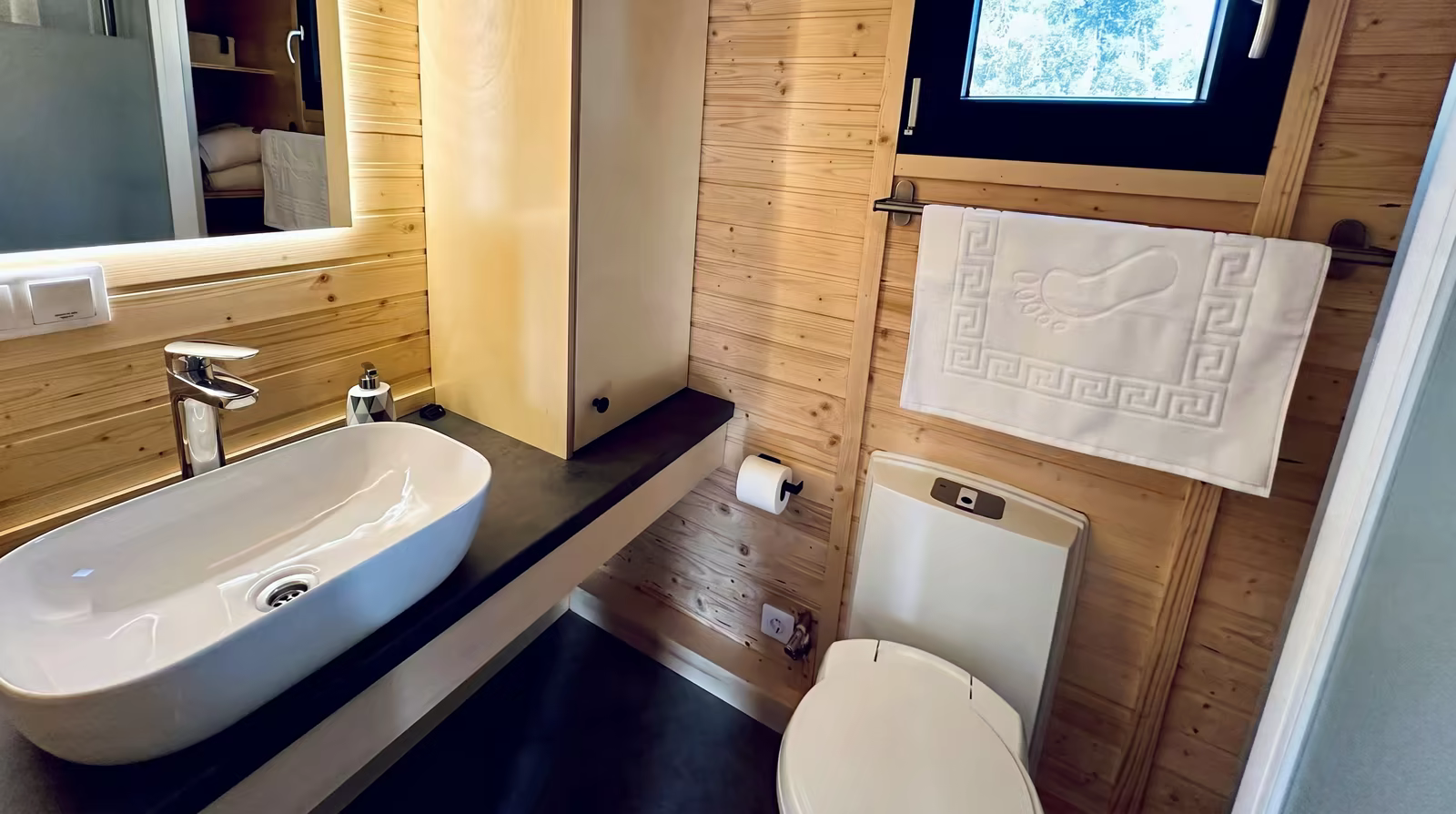Bagno con lavabo, specchio illuminato, WC e una piccola finestra