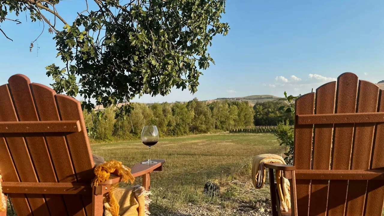 Due sedie da giardino rivolte verso prato e colline, con un calice di vino