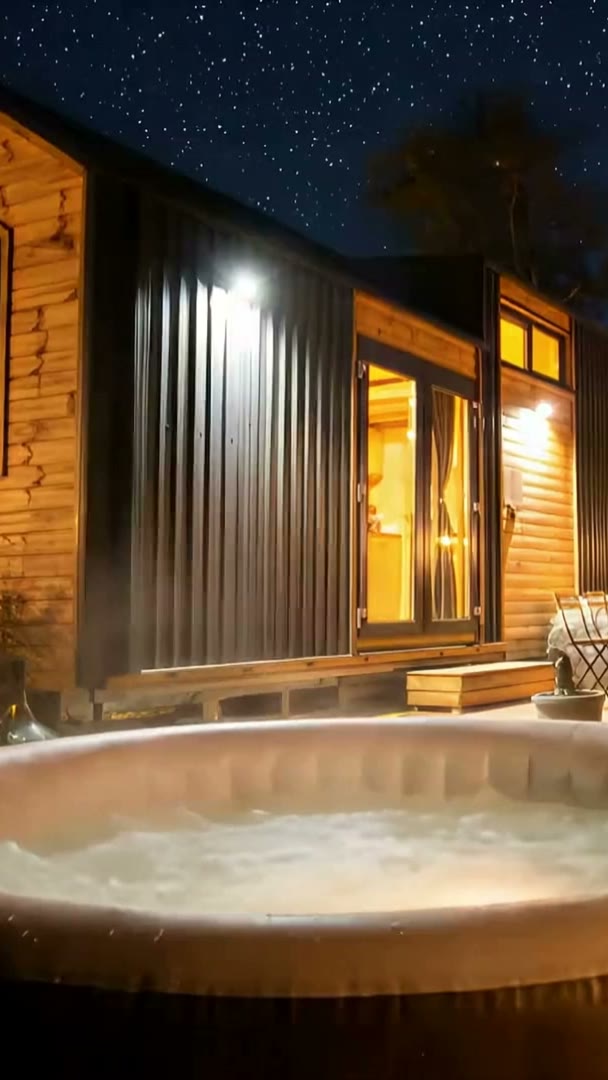Casetta di legno illuminata di notte, con una vasca idromassaggio davanti